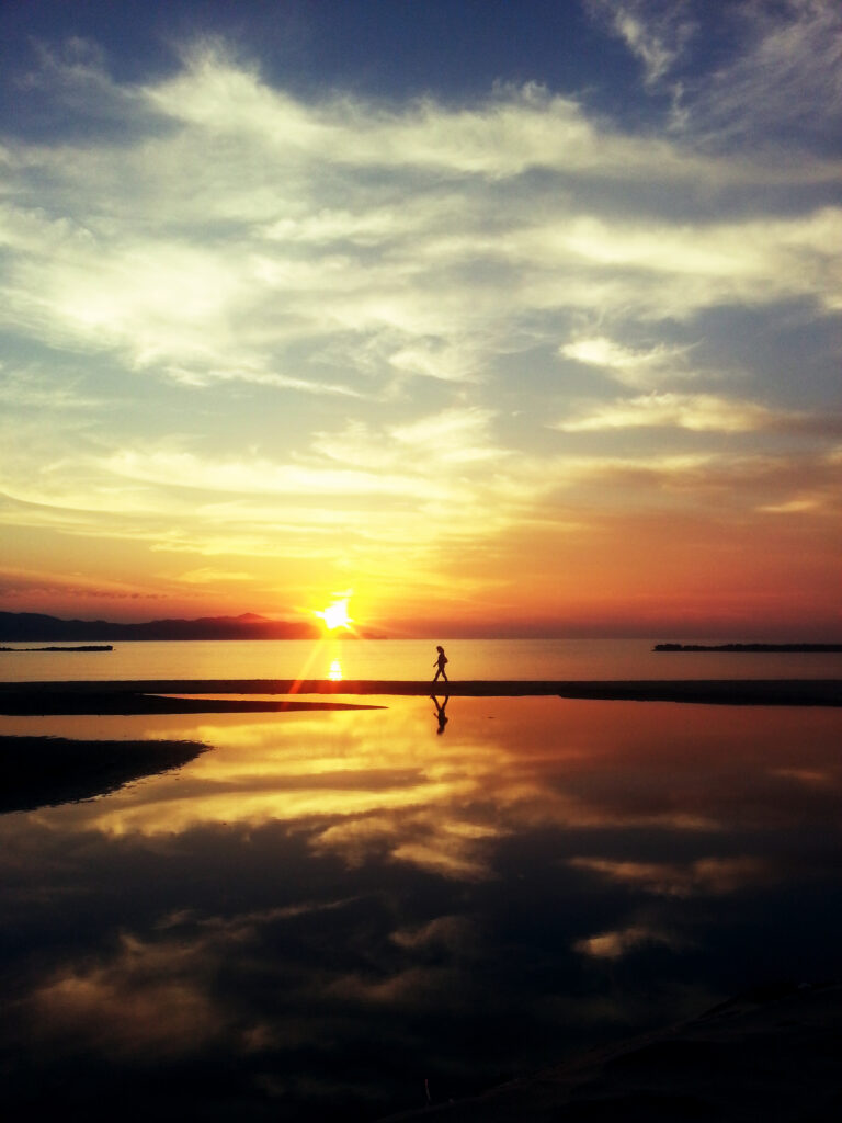 A person walking by the ocean at sunset