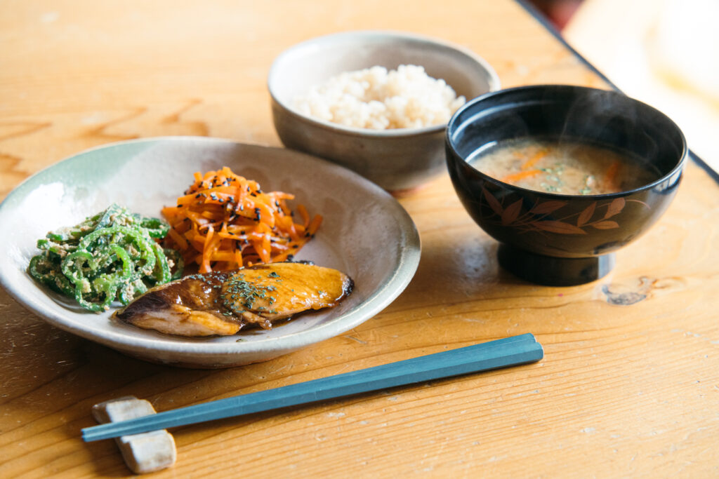 A Japanese meal featuring rice, miso soup, vegetables, and fish.