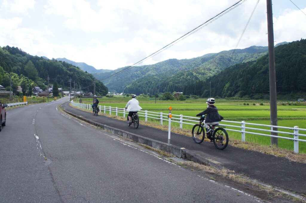Cyclists begin their tour, riding e-bikes on a path through Ayabe's scenic rice paddies and mountains.