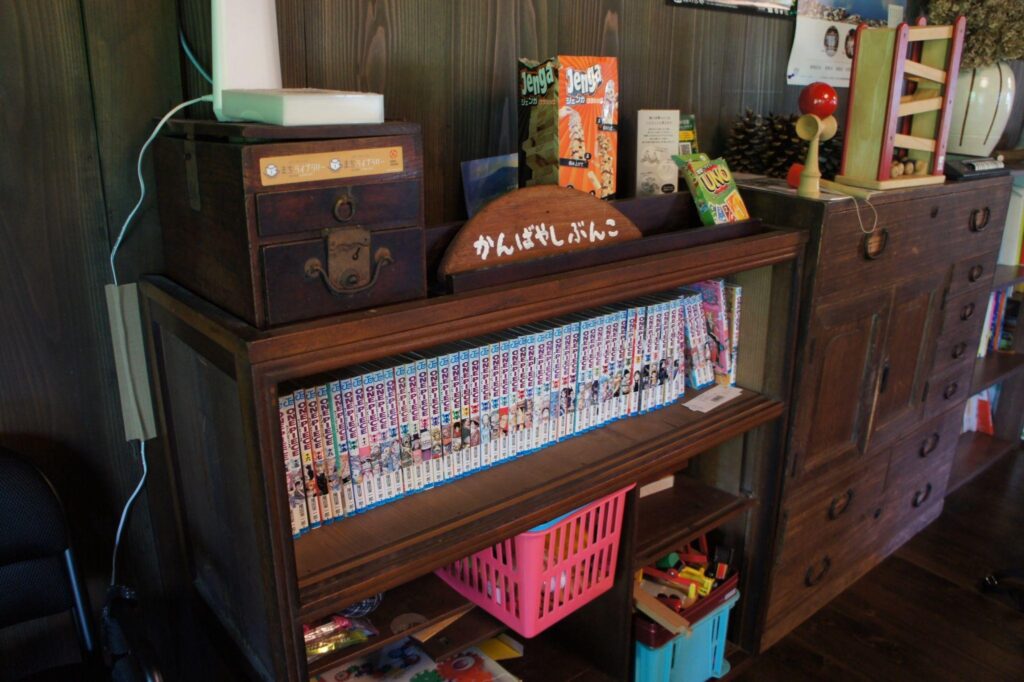 A cozy corner inside Nio no Sumika, with a bookshelf full of manga comics and a collection of retro games and toys.
