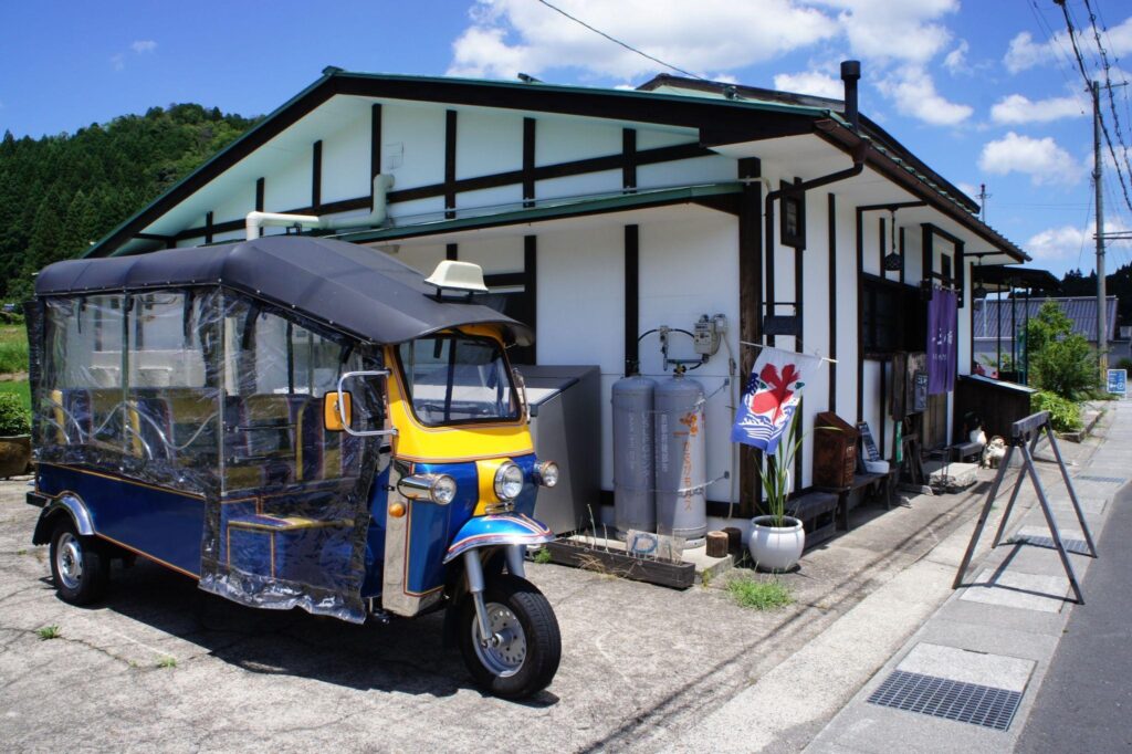 A colorful blue and yellow tuk-tuk parked outside the Nio no Sumika cafe in the Japanese countryside.
