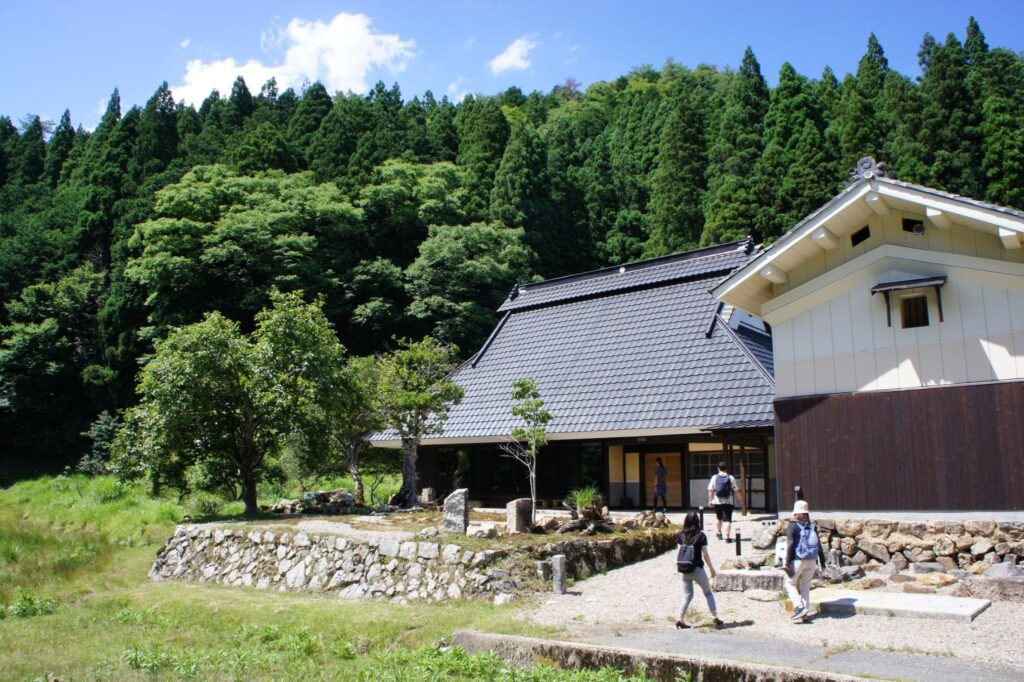 Visitors walk towards the traditional Nio no Yado Komura guesthouse, a tranquil lodging at the foot of a lush forest.