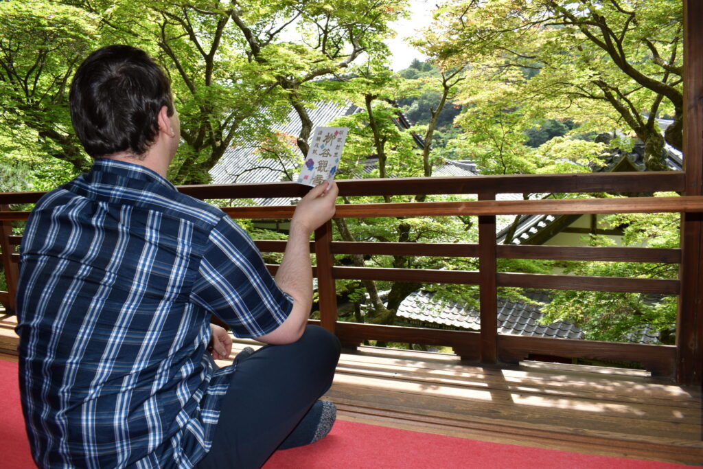 Tourist admires the green maples of Yokokuji Temple from the Kamishoin while holding a goshuin seal.