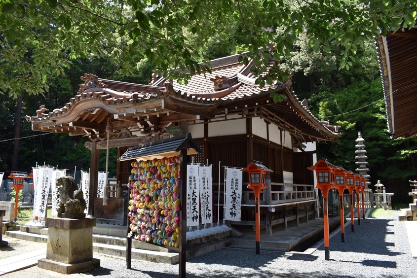 Temple in Kyoto surrounded by green maple leaves with banners and flowers near the entrance.